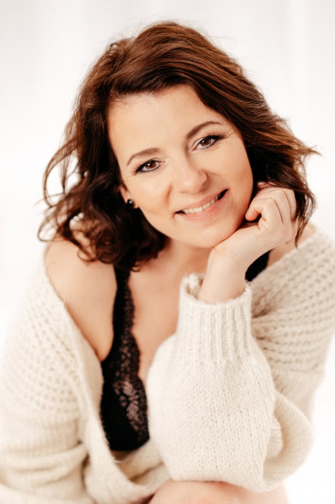 Strahlendes Lächeln einer Frau bei einem Boudoir-Shooting in entspannter Atmosphäre - Dein Boudoir Frau lächelt freundlich in die Kamera, trägt einen weißen Pullover und schwarze Spitze, wirkt selbst.