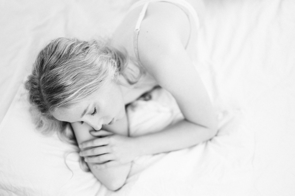 Schlafende Frau liegt friedlich auf einem Bett, eingekuschelt in weiße Bettwäsche.