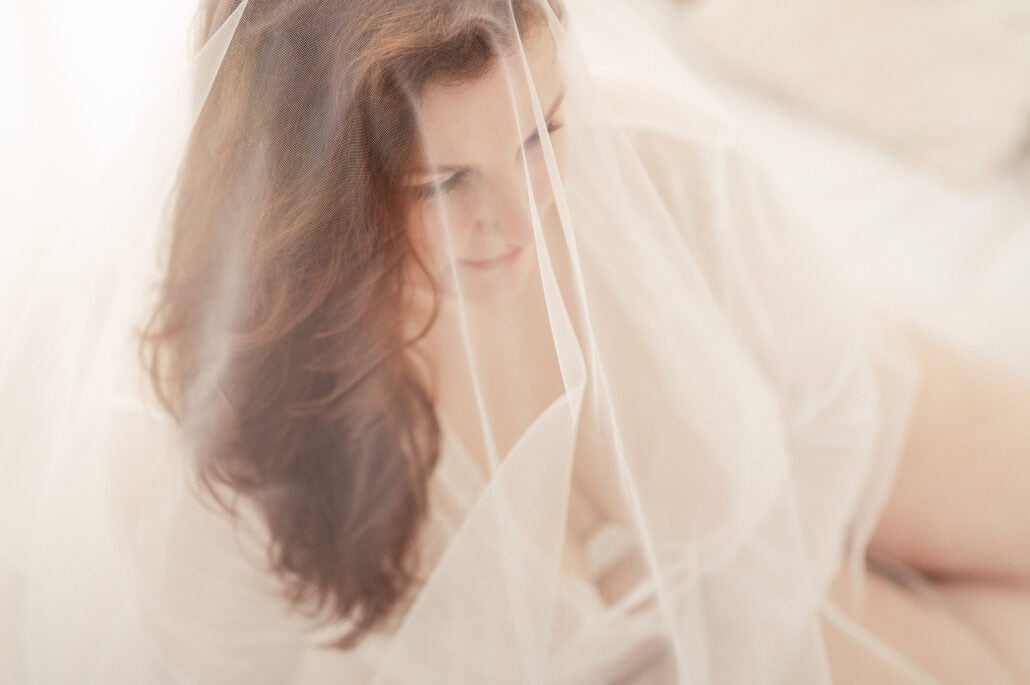 Close-up of a bride with a sheer veil over her face, in soft lighting.