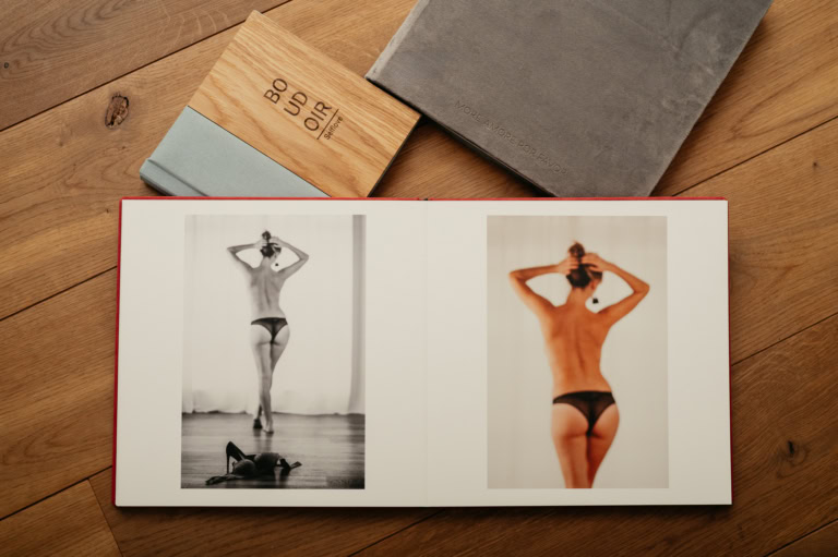 Open book on a wooden table showing a two-page fashion spread: left is a black-and-white back view of a model, right is a color back view in underwear/lingerie.