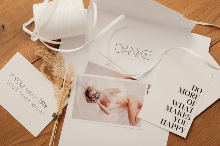 Overhead view of white gift cards and photos scattered on a wooden table with dried grasses and ribbons.