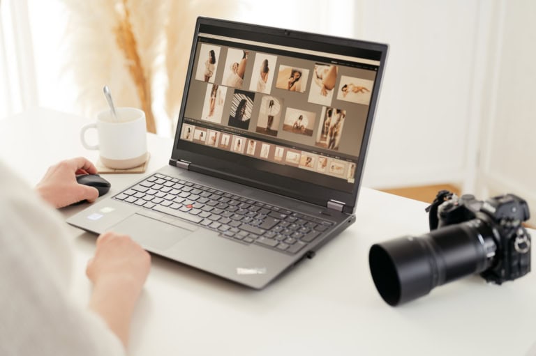 Person uses a laptop displaying a grid of fashion photos; a camera sits on the desk nearby with a mug to the side.