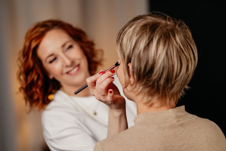 Makeup artist applies eye makeup to a client's eye with a brush in a studio. (close-up)