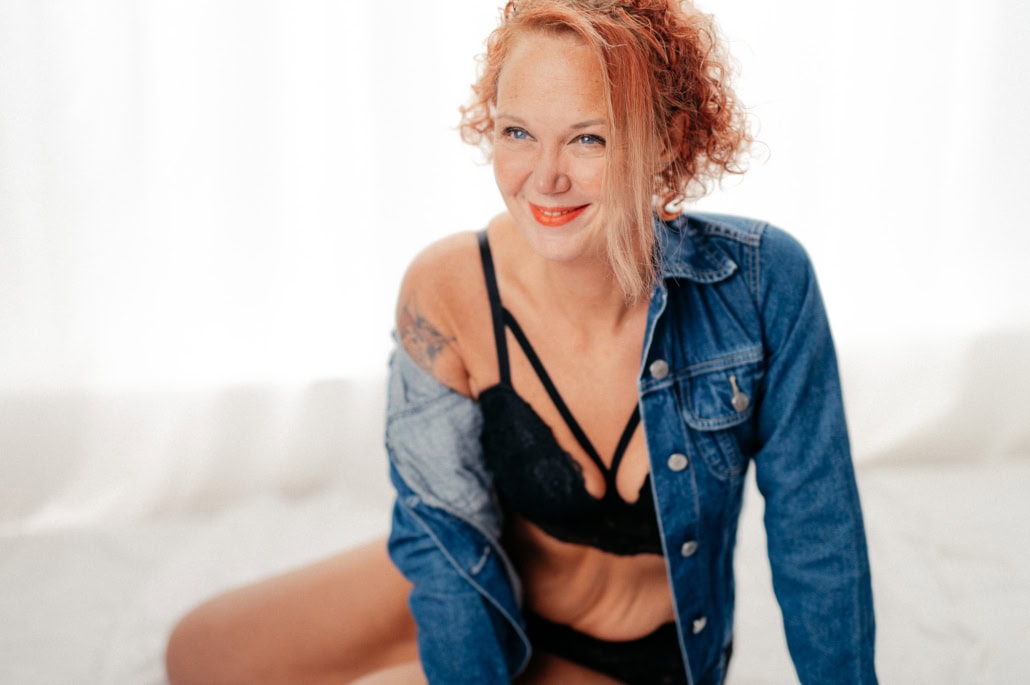 Schönes Boudoir-Foto einer lächelnden Frau mit roten Locken in Dessous und Jeansjacke - Dein Boudoir Lächelnde Frau in Dessous und Jeansjacke bei einem Boudoir-Shooting, entspannt und selbstbewusst.