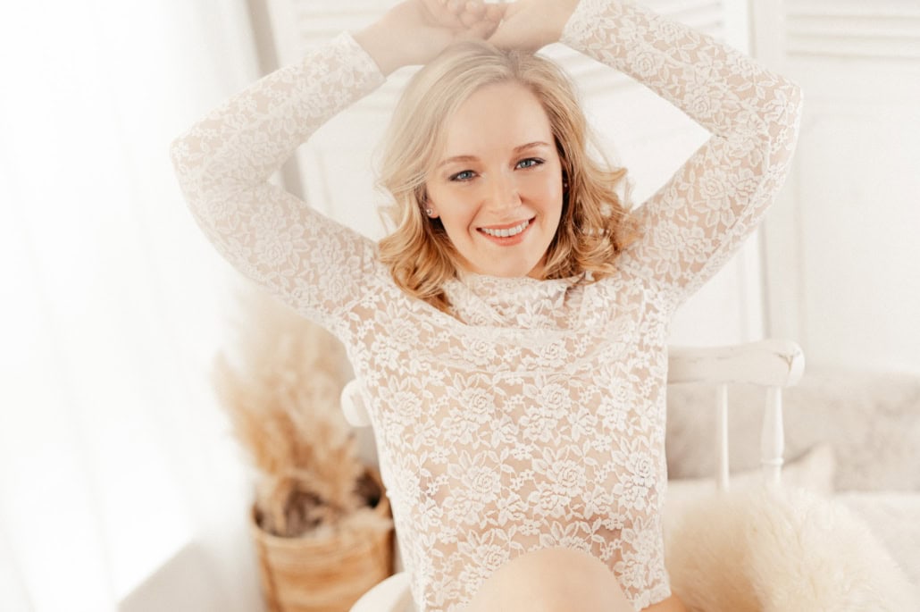 Entspannte junge Frau in Spitzenkleid, lachend und glücklich, in hellem Wohnzimmer mit natürlichem L.