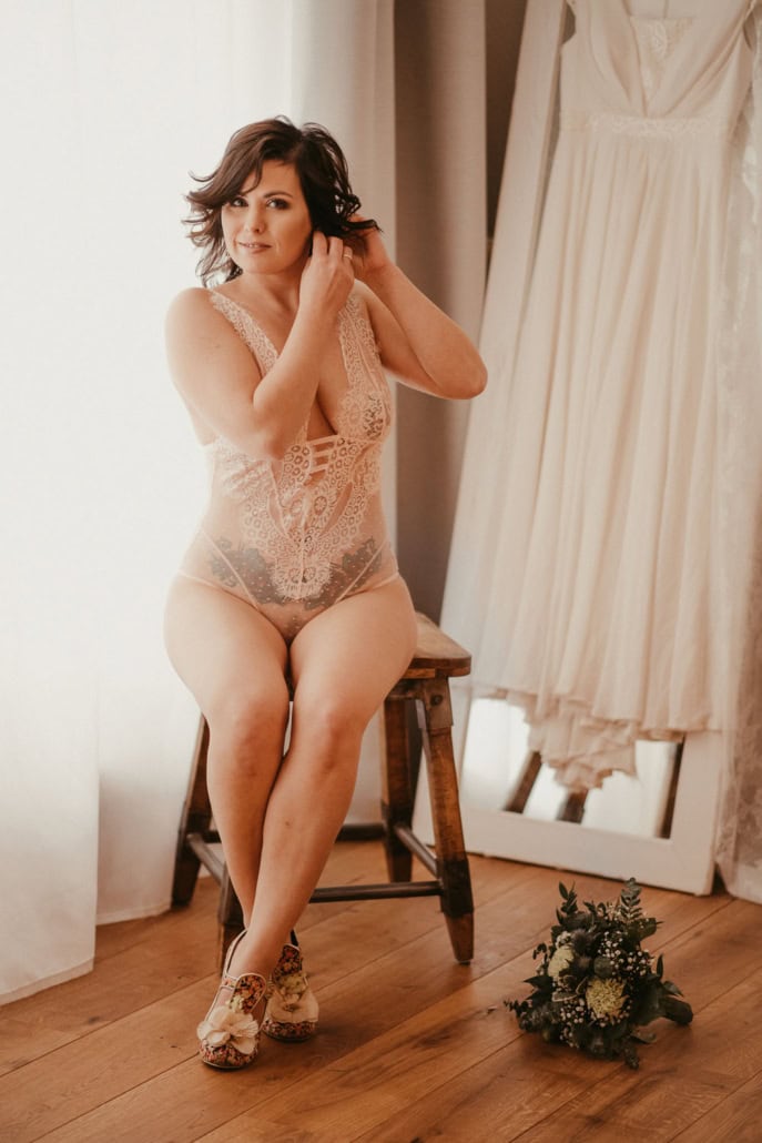 Zarte Boudoir-Fotografie einer Frau in Spitze, sitzend auf einem Stuhl im Schlafzimmer. - Dein Boudoir Frau in eleganter Spitzen-Boudoir-Kleidung, entspannt und selbstbewusst.