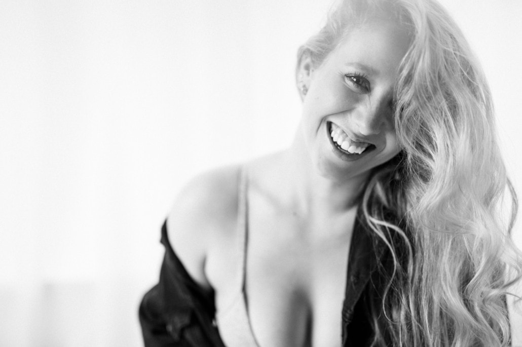 Porträt einer lachenden Frau in sinnlicher Boudoir-Atmosphäre, Schwarz-Weiß-Fotografie - Dein Boudoir Sinnliches Boudoir-Portrait einer lachenden Frau mit lockigem Haar, schwarz-weiß, intime Atmosphäre.