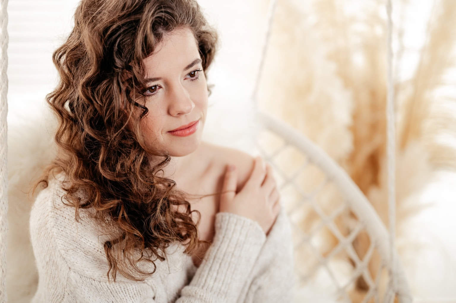 Porträt einer jungen Frau mit lockigem Haar, die nachdenklich in die Kamera schaut. - Dein Boudoir Junge Frau mit lockigem Haar in einem gemütlichen Raum, wirkt nachdenklich und entspannt.