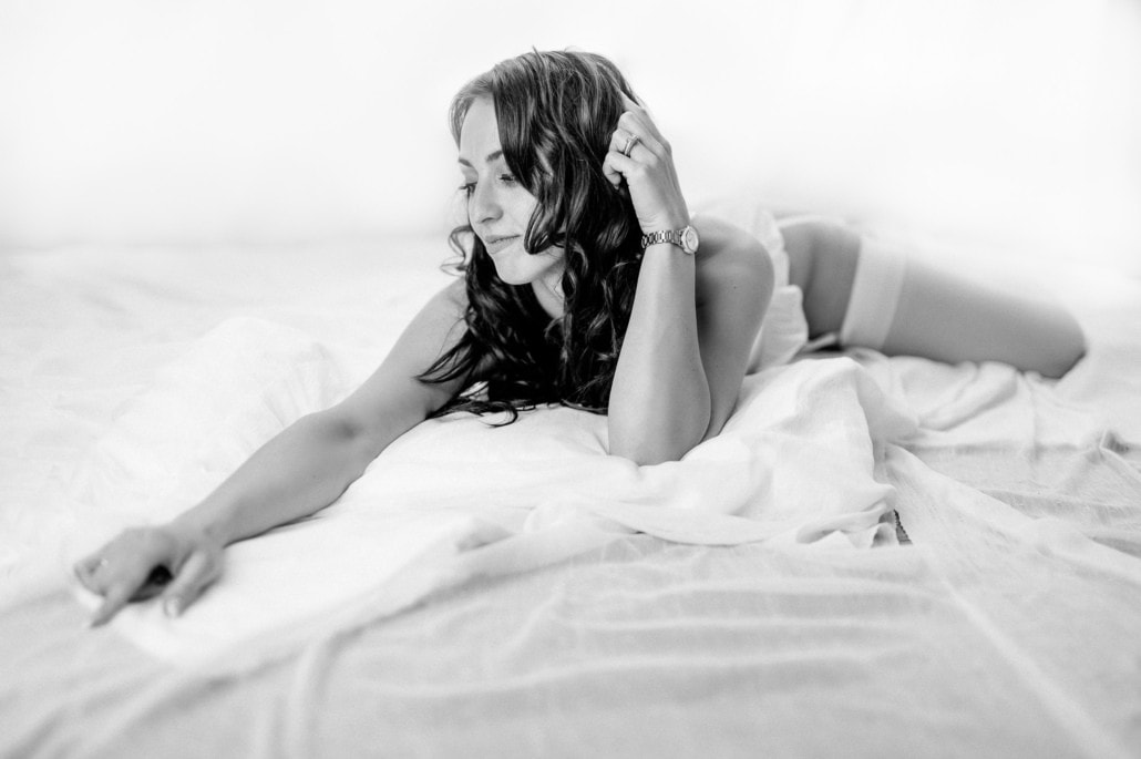 Sinnliches Boudoir-Foto einer Frau auf Bett, entspannte Pose, intime Atmosphäre, elegante Stimmung.