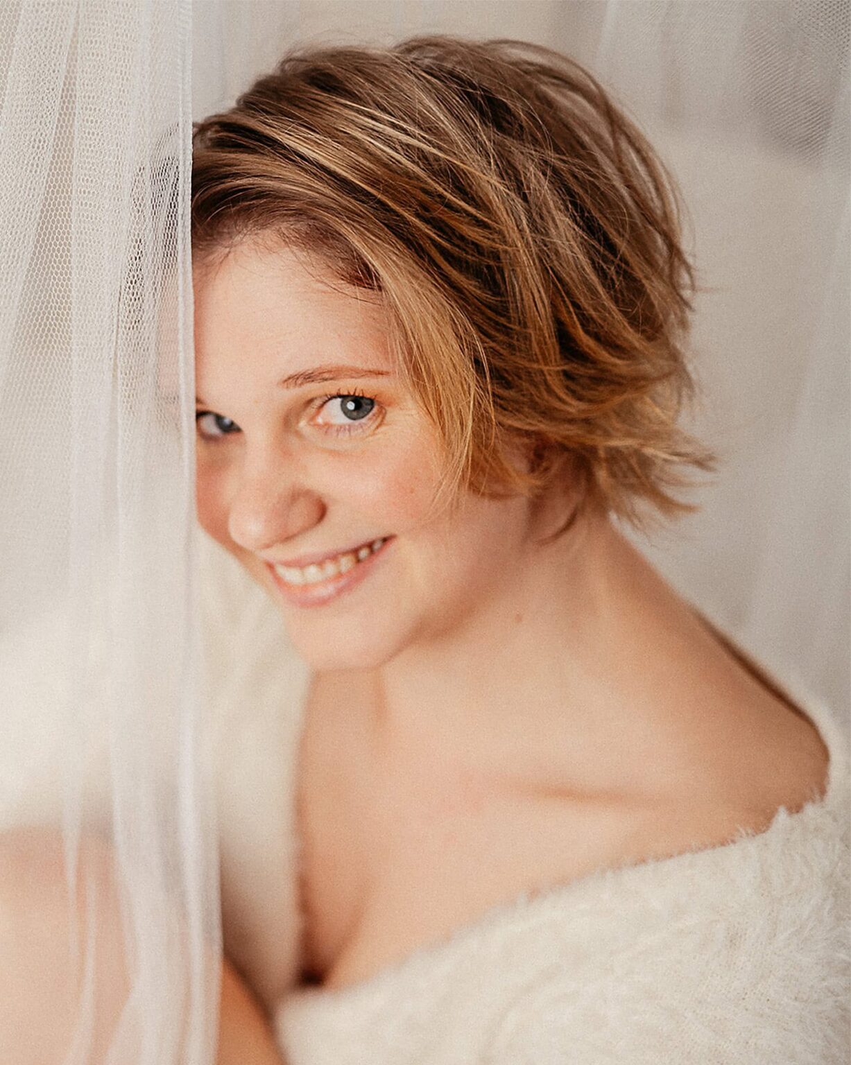 Frau mit kurzen Haaren, lachend, im Boudoir-Stil, natürlicher Look, warmes Licht.